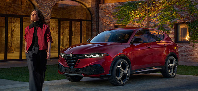 Un Alfa Romeo Tonale Sport Speciale 2026 rojo estacionado en un patio, con una mujer alejándose del vehículo.