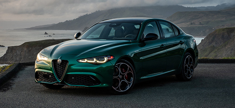 A driver-side front angle of a green 2026 Alfa Romeo Giulia Veloce parked on a rocky beach.