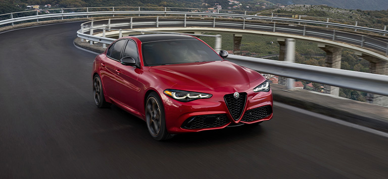 A red 2026 Alfa Romeo Giulia Veloce taking a curve on an elevated highway.