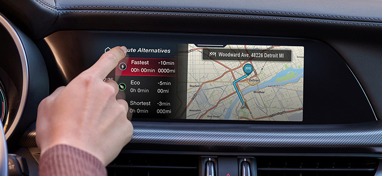 The Uconnect touchscreen and heating and cooling vents in a 2026 Alfa Romeo Stelvio with the driver touching the screen.