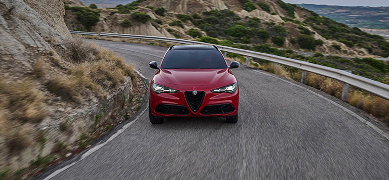 A red 2026 Alfa Romeo Stelvio Veloce traveling down a winding mountain road.