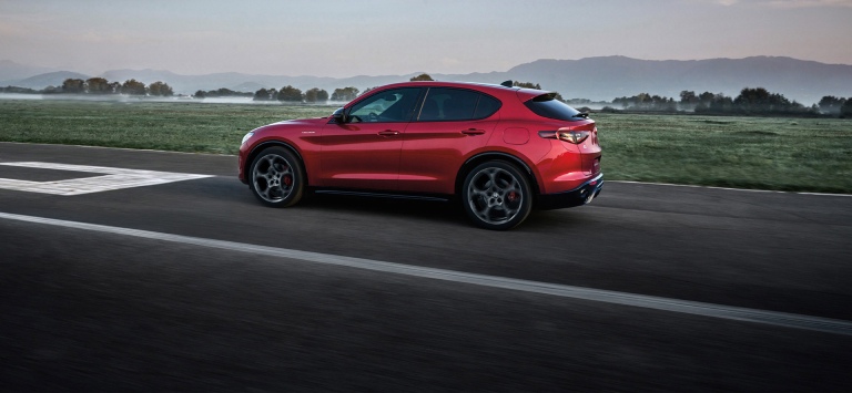 A rear angle of a red 2026 Alfa Romeo Stelvio Veloce traveling on a snow-covered road.